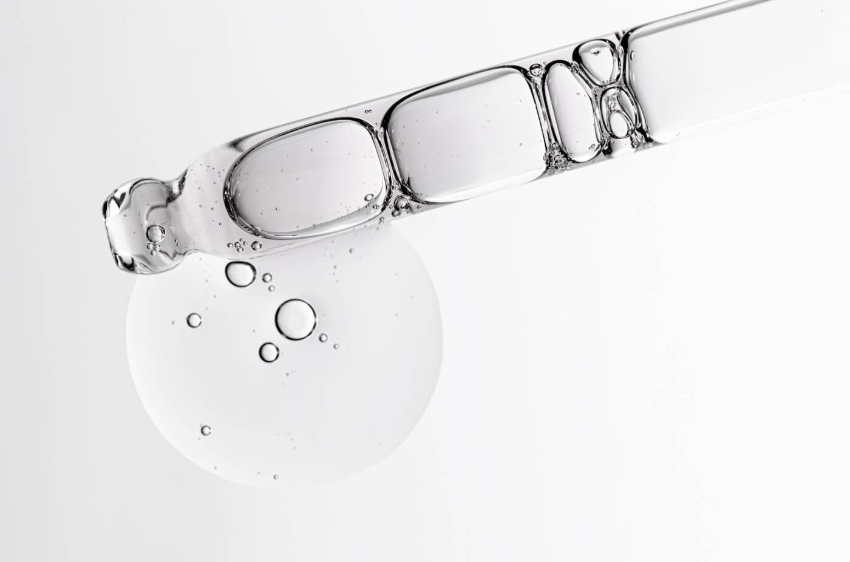 Szklana pipeta z przezroczystym serum, z którego spływa kropla płynu z widocznymi pęcherzykami powietrza na jasnym tle