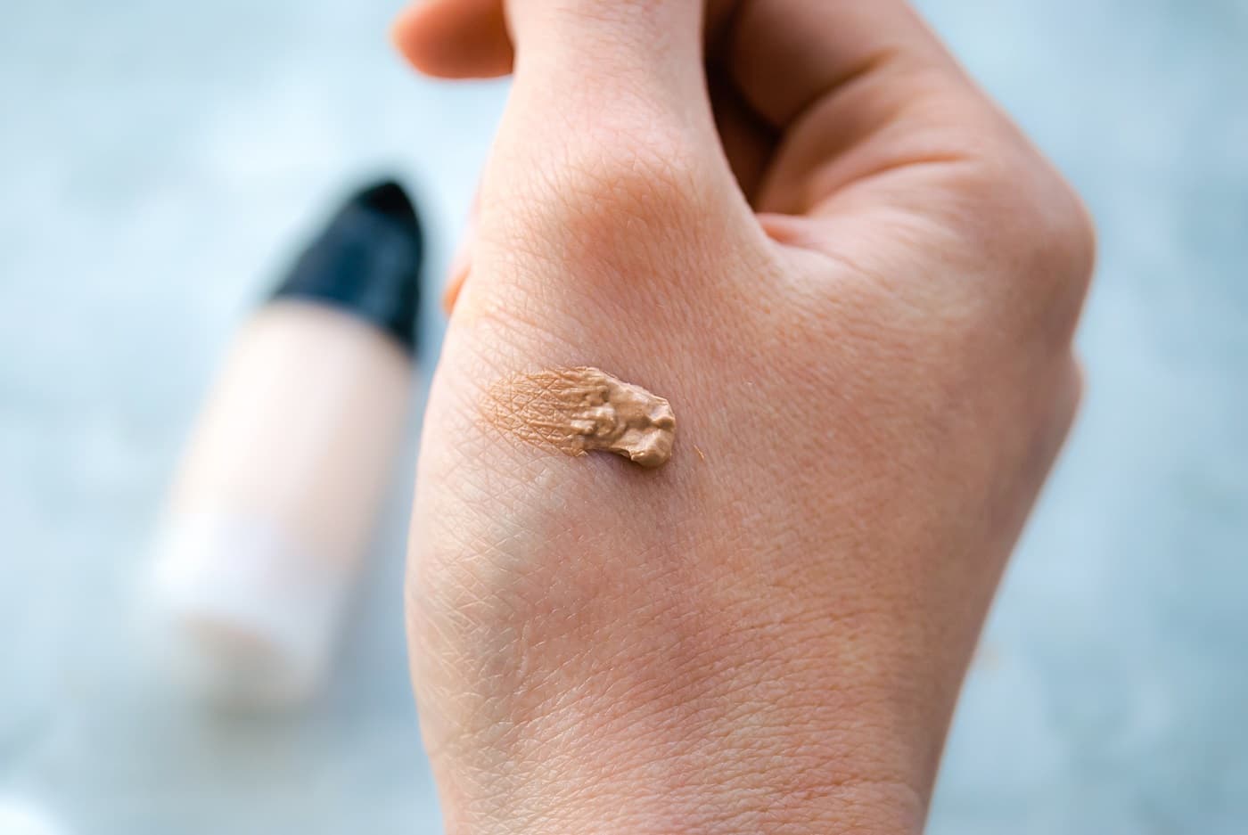 SPF z kolorem na dłoni, a w tle flakon produktu kolorowego z filtrem UV.