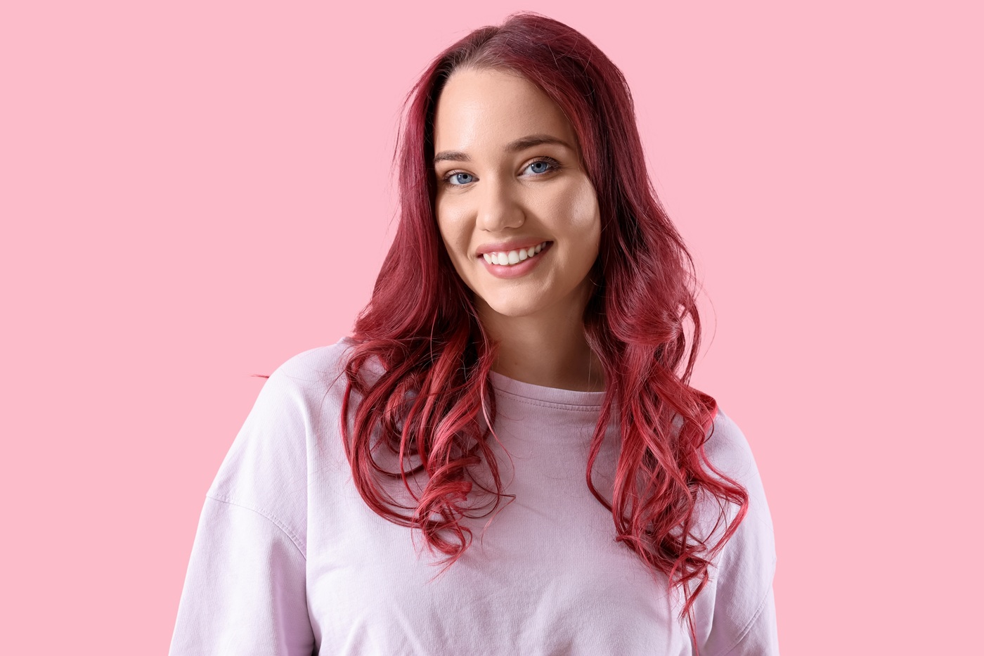 Piękna młoda kobieta z burgundowymi włosami na różowym tle