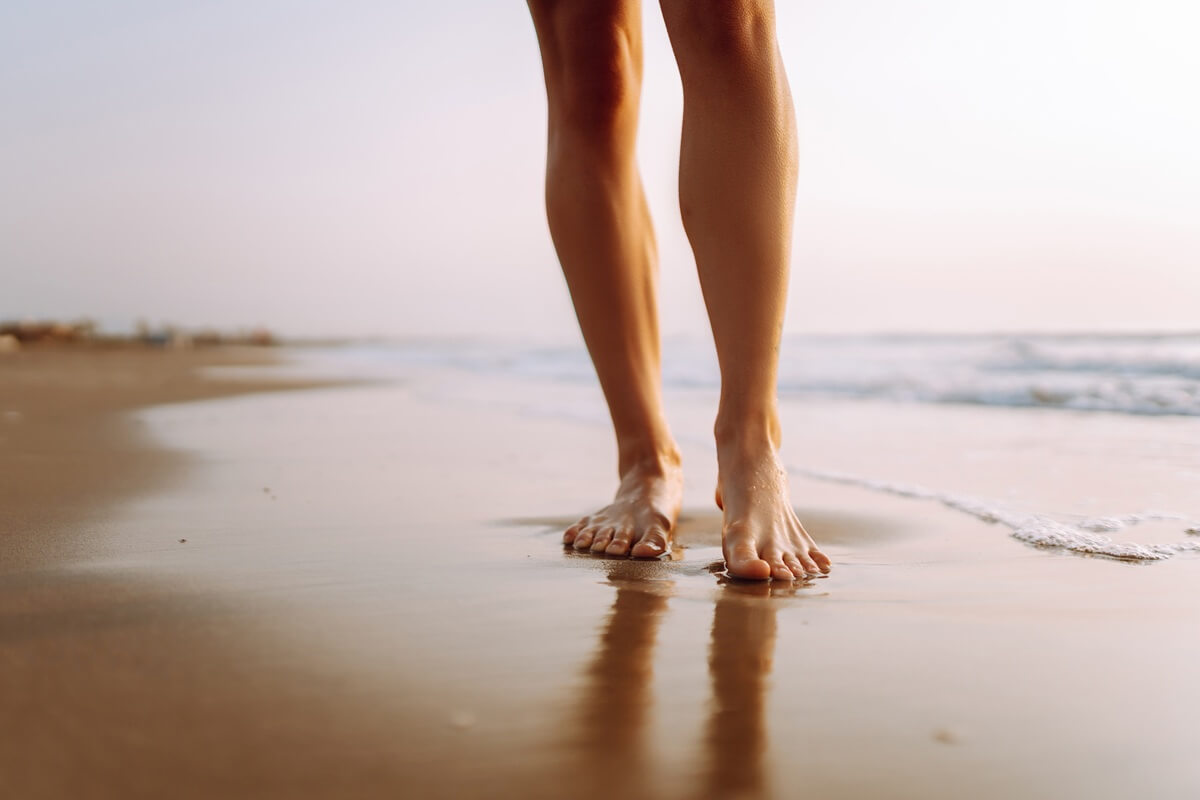 Zbliżenie na nogi, które są na brzegu piaszczystej plaży.