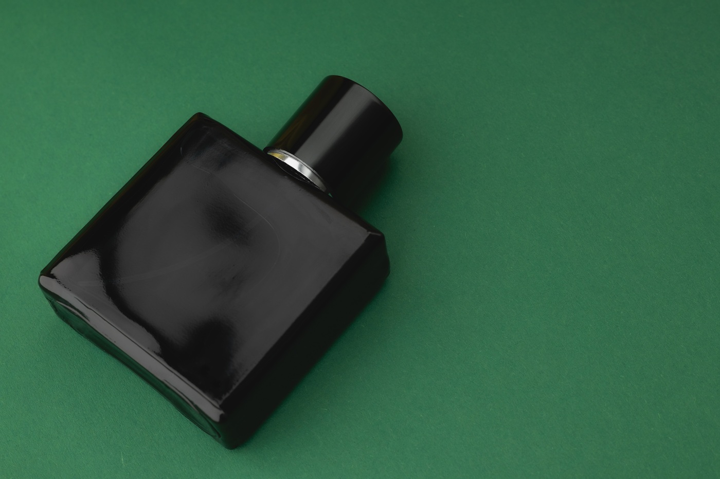 Czarny flakon perfum na ciemnozielonym tle.