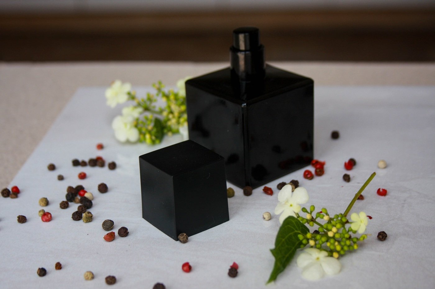 Czarny flakon perfum w otoczeniu ziaren pieprzu i kwiatów