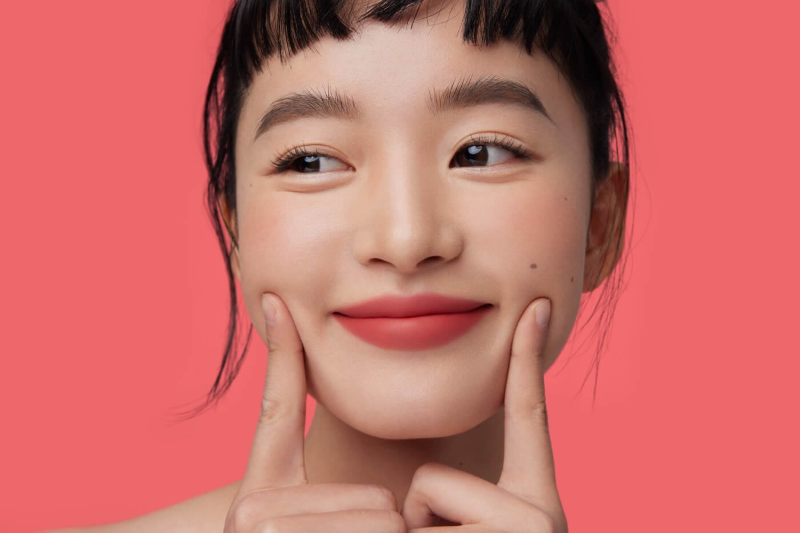 Młoda, uśmiechnięta Koreanka z piękną cerą po zastosowaniu koreańskiej maski na twarz.