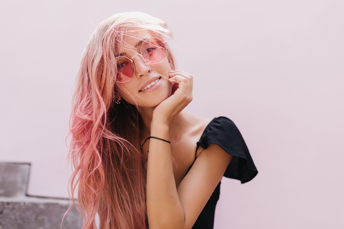 Młoda kobieta z długimi, pastelowo różowymi włosami opiera głowę na dłoni i patrzy w obiektyw