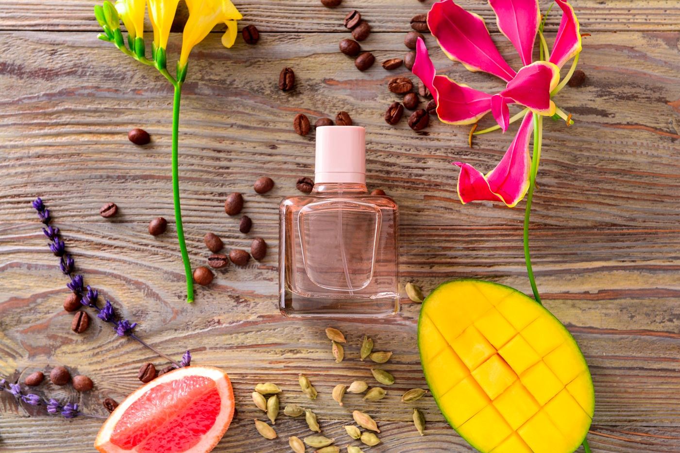 Butelka perfum otoczona mango, grejpfrutem, kwiatami i ziarnami kawy na drewnianym tle