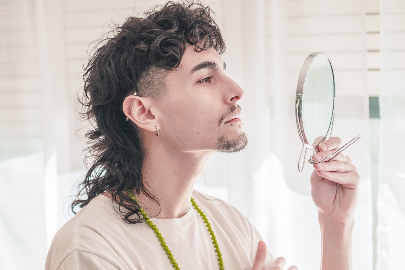 Mężczyzna z kręconą fryzurą typu mullet przegląda się w ręcznym lusterku