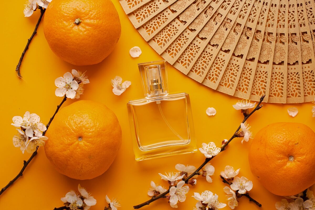 Perfumy pomarańczowe w otoczeniu owoców i kwiatów pomarańczy.