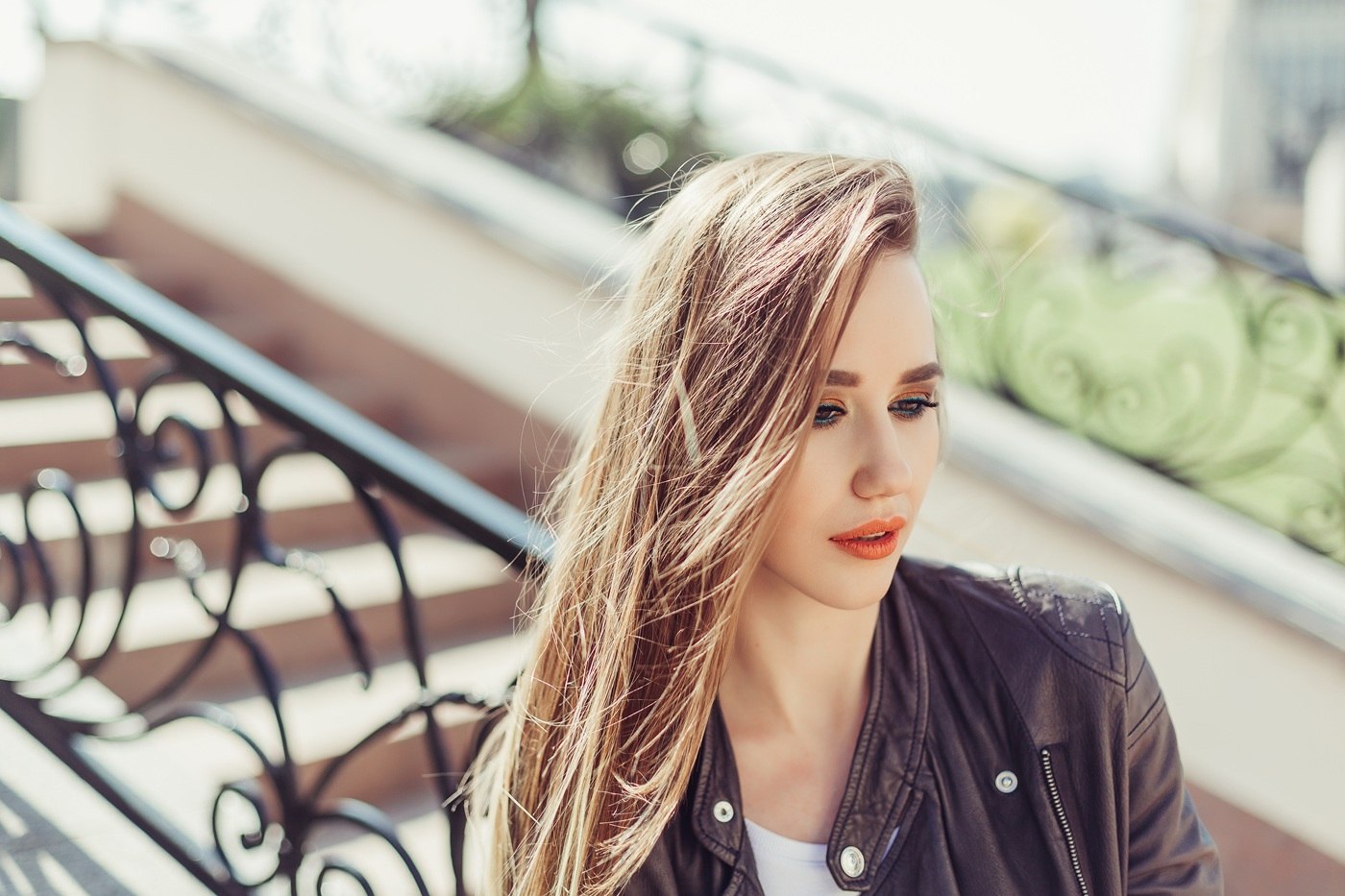 Młoda kobieta o jasnych włosach siedzi na schodach w słoneczny dzień.