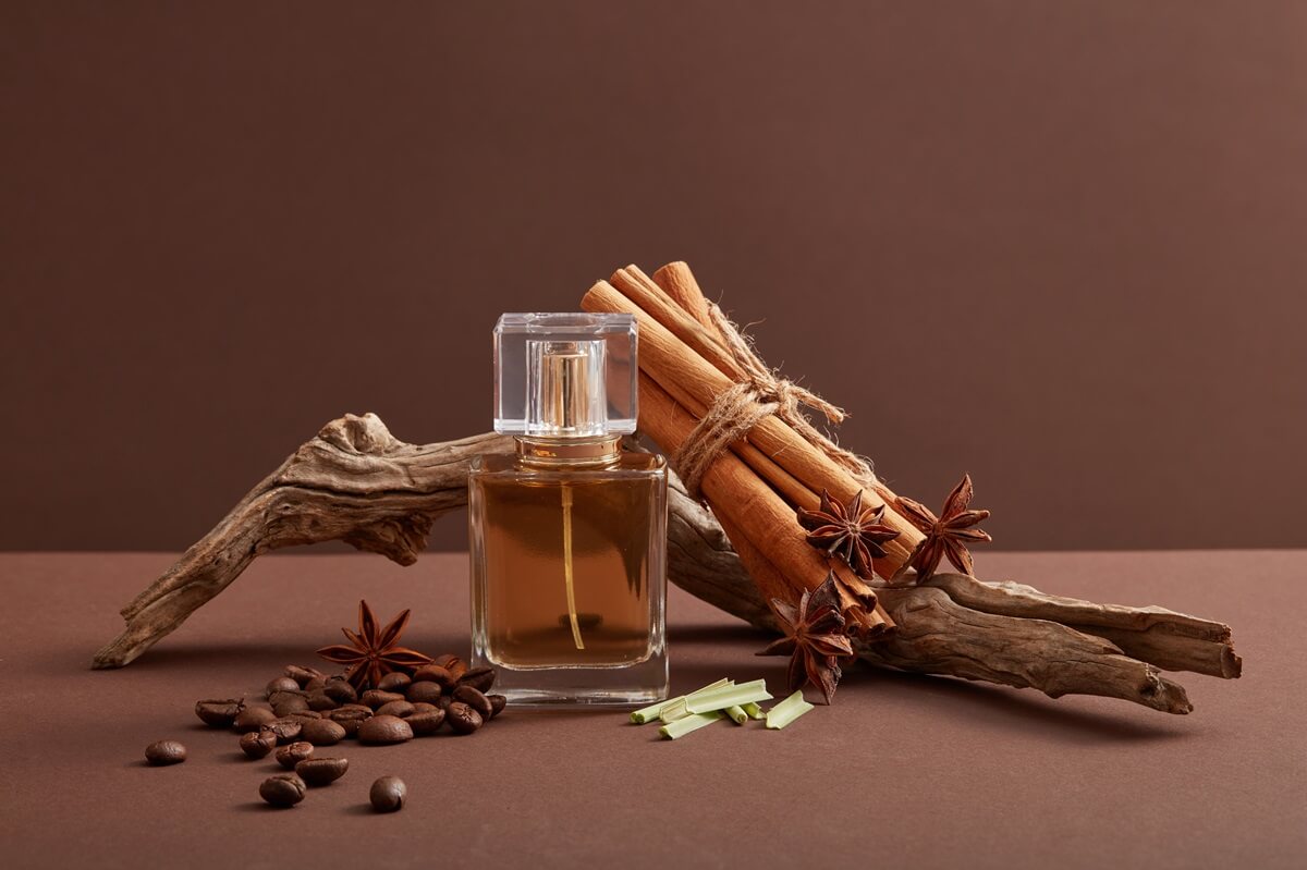 Perfumy cynamonowe w otoczeniu korzennych przypraw na brązowym, ciepłym tle.