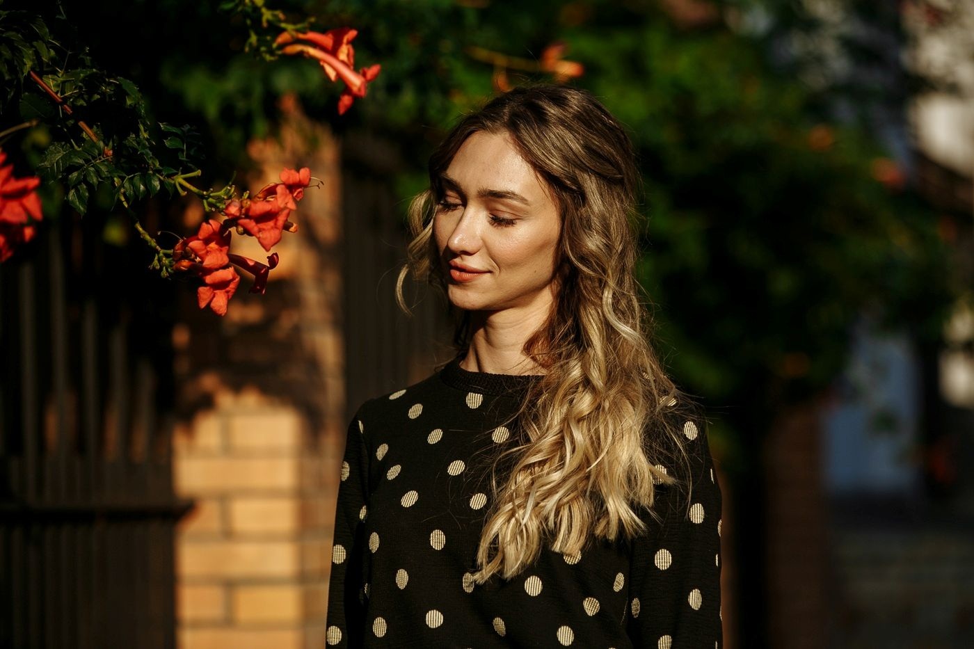 Młoda kobieta z długimi włosami z jasnymi refleksami stoi na zewnątrz w ciepłym świetle słońca