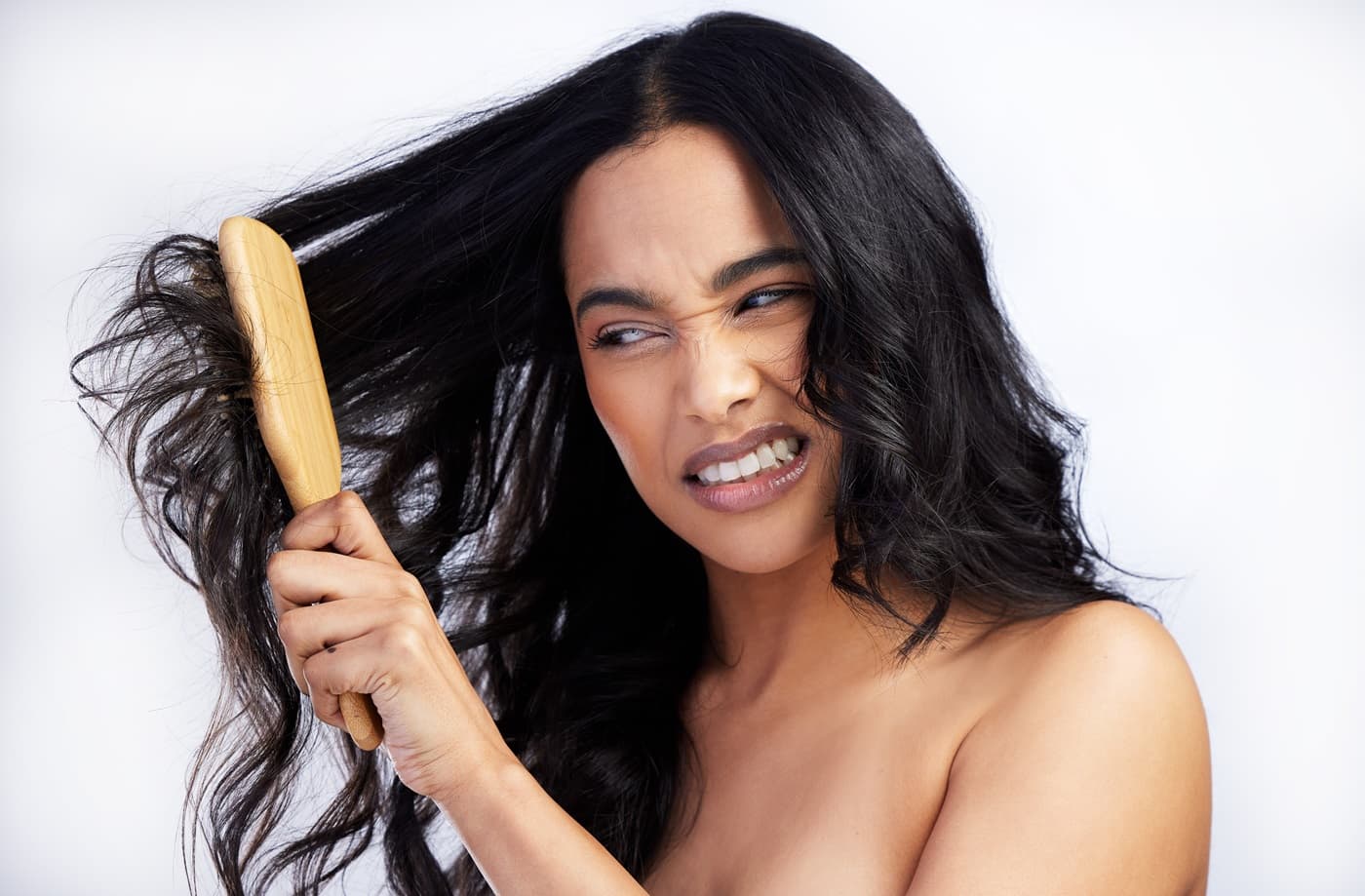 Młoda kobieta próbuje rozplątać kołtuny we włosach za pomocą drewnianej szczotki.