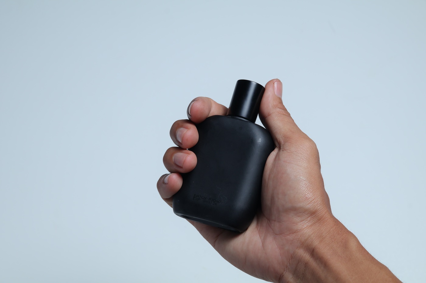 Męska dłoń trzymająca czarny flakon perfum do 200 zł.