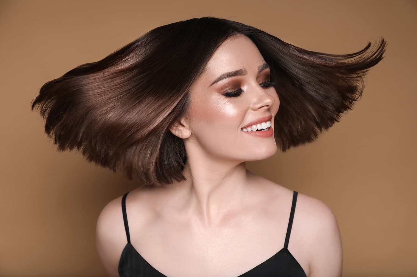 Młoda, uśmiechnięta kobieta z rozwianymi, krótki włosami po dekoloryzacji.