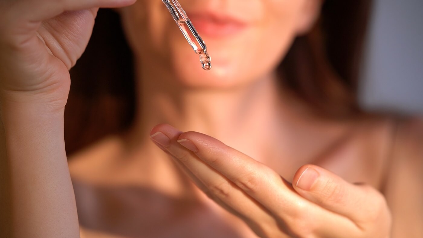 Kobieta nakłada serum z pipety na skórę twarzy w codziennej pielęgnacji.