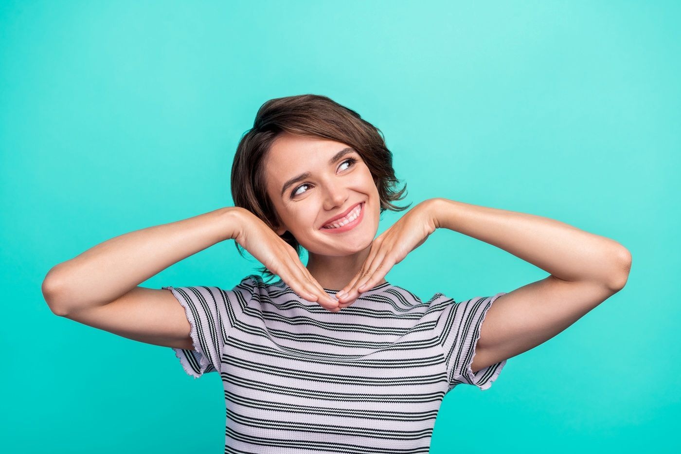 Uśmiechnięta młoda kobieta z krótkimi brązowymi włosami pozuje na tle turkusowego tła