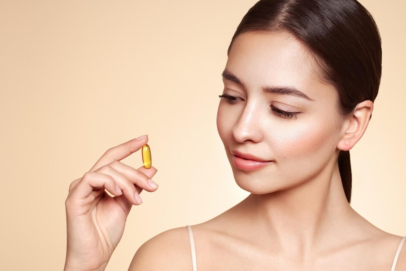 Młoda kobieta trzymająca w ręku kapsułkę z witaminą D.