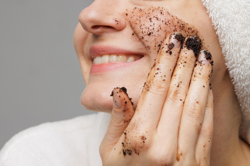 Zbliżenie na dłoń kobiety i jej lewy bok twarzy, na którym wykonuje peeling mechaniczny.