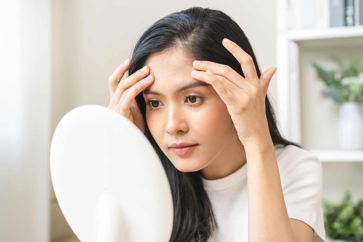 Młoda kobieta przygląda się w lusterku swojej skórze.