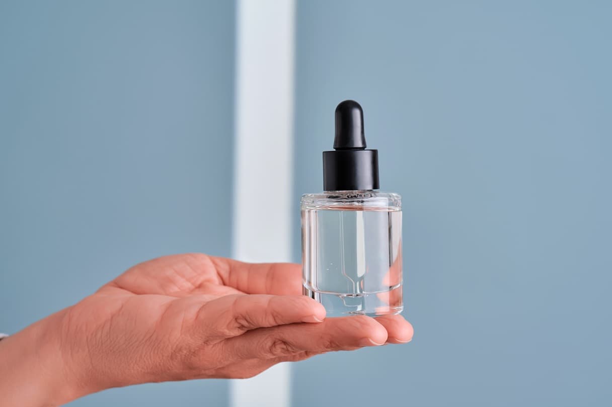 Dłoń trzymająca przezroczyste serum z szklanej butelce z pipetą.