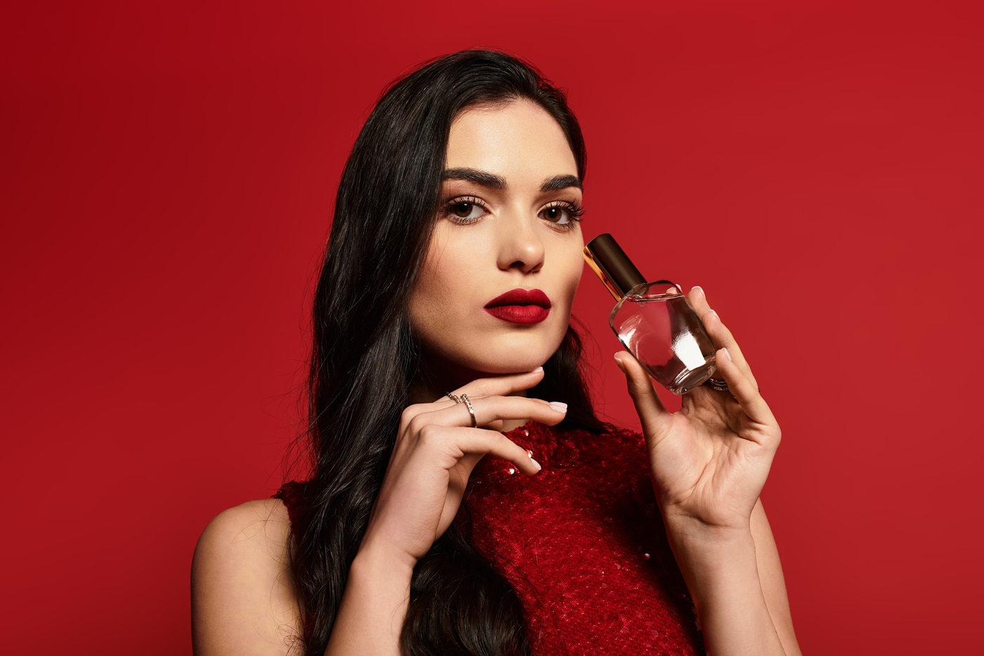 Kobieta na czerwonym tle trzyma flakon mocnych perfum.