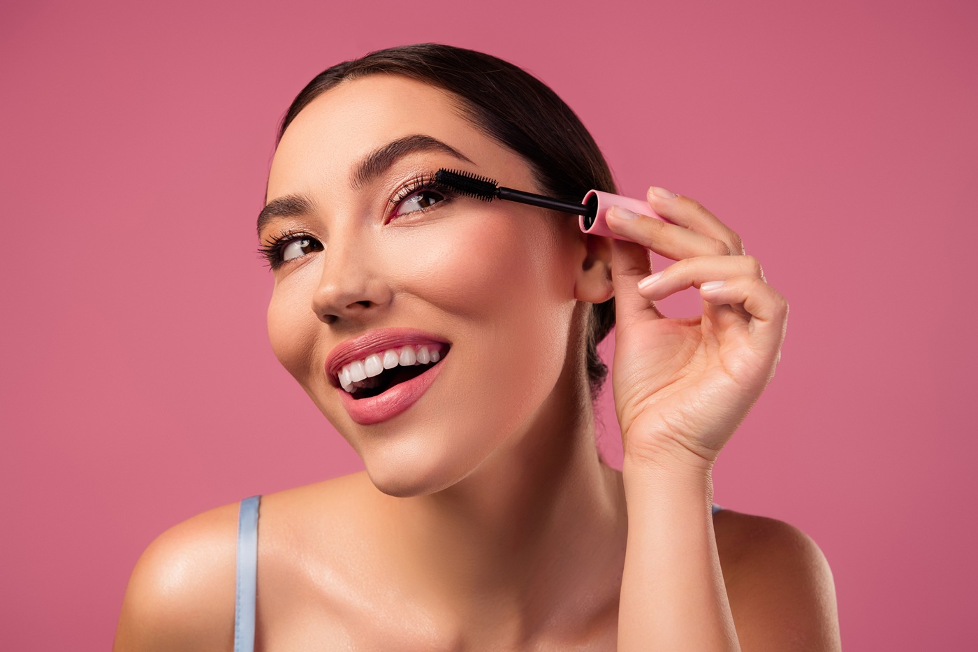 Młoda uśmiechnięta kobieta nakłada tusz do rzęs na górne rzęsy