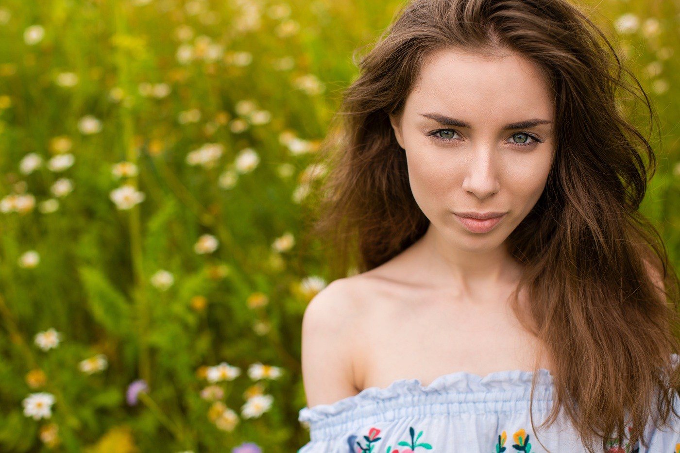 Młoda kobieta z długimi, brązowymi włosami stoi na łące pełnej kwiatów