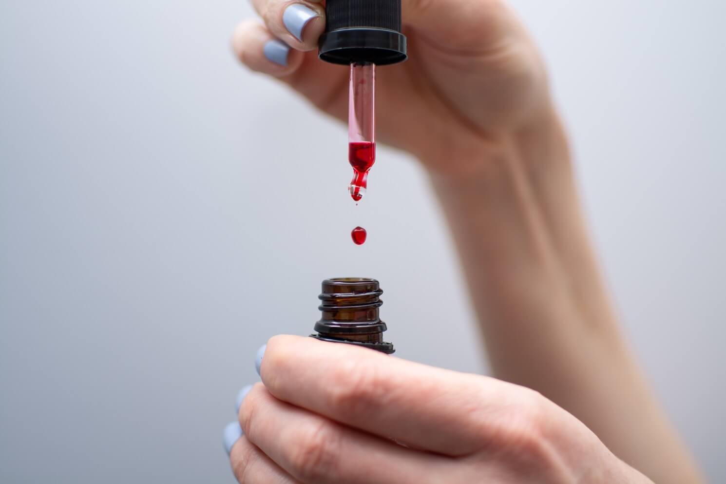 Kropla czerwonego serum z witaminą B12 spadająca z pipety do brązowej buteleczki trzymanej w dłoni.