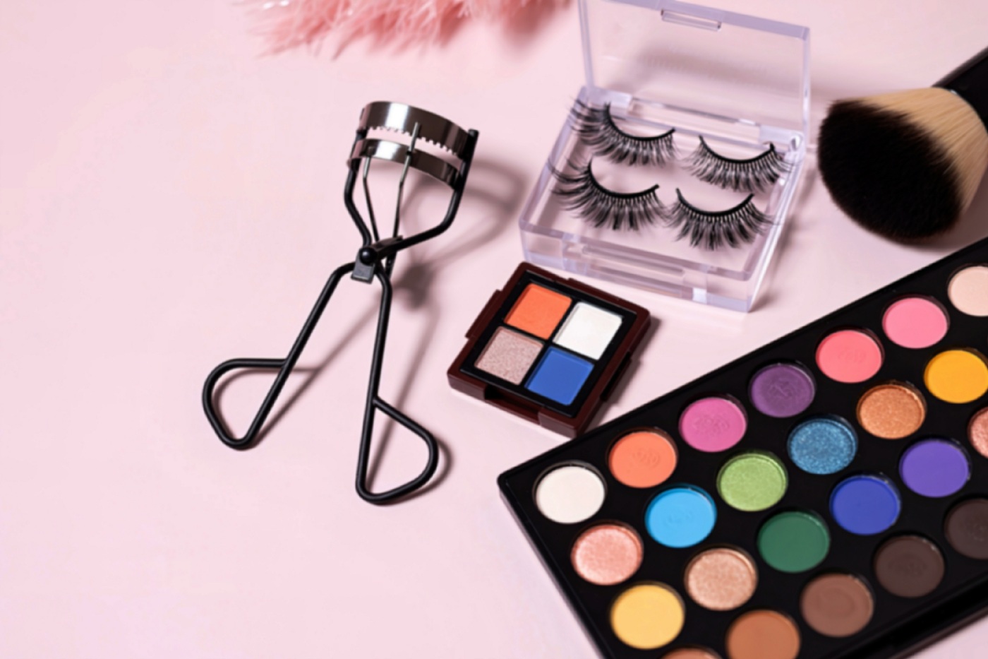 Sztuczne rzęsy w pudełku obok zalotki, palety kolorowych cieni do powiek, pędzla do makijażu i kosmetyków