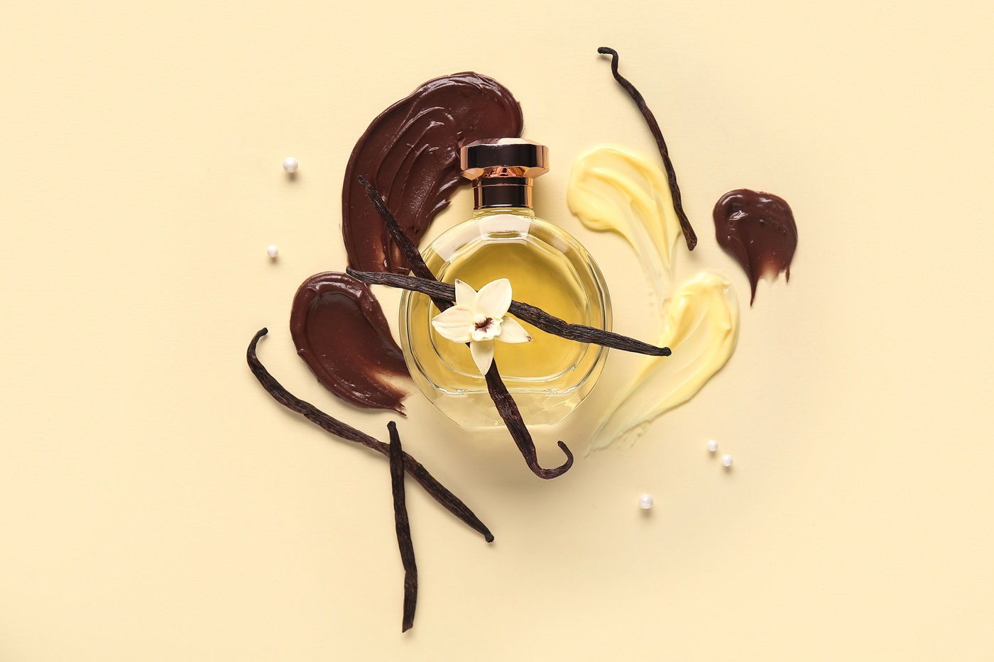 Flakon perfum otoczony nutami wanilii i czekolady - laski wanilii, kremowe i czekoladowe akordy na jasnym tle.