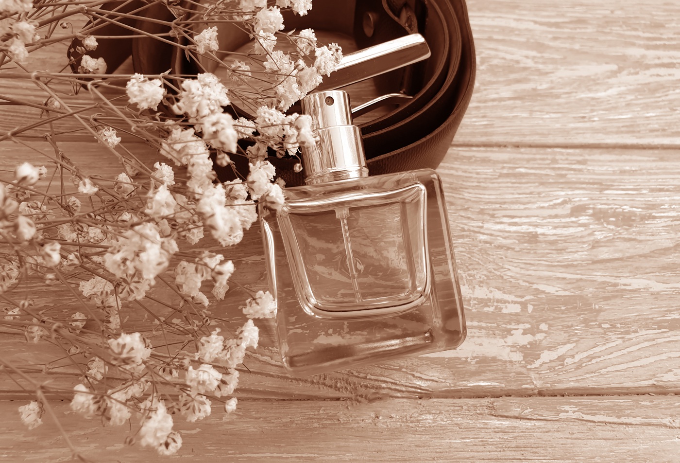 Flakon perfum na tle drewna, kwiatów i skórzanego paska