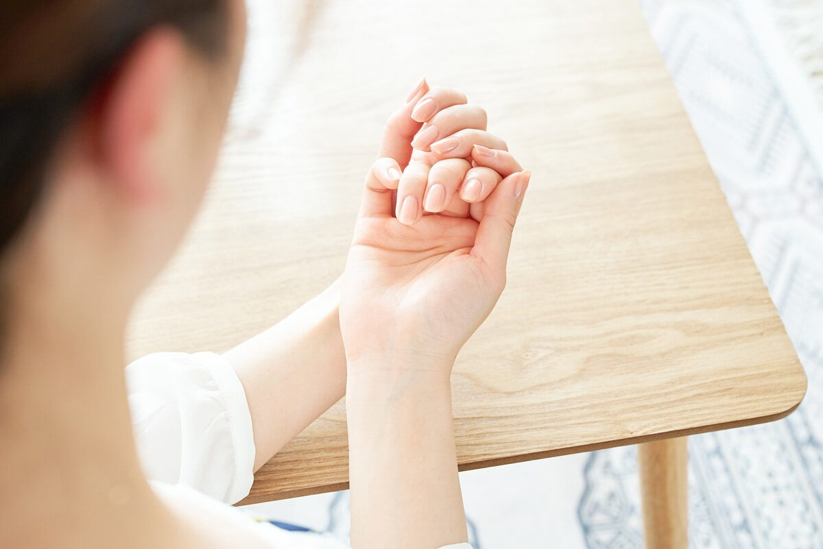 Widok z tyłu na kobietę oglądającą swoje dłonie z naturalnymi, jasnymi paznokciami.