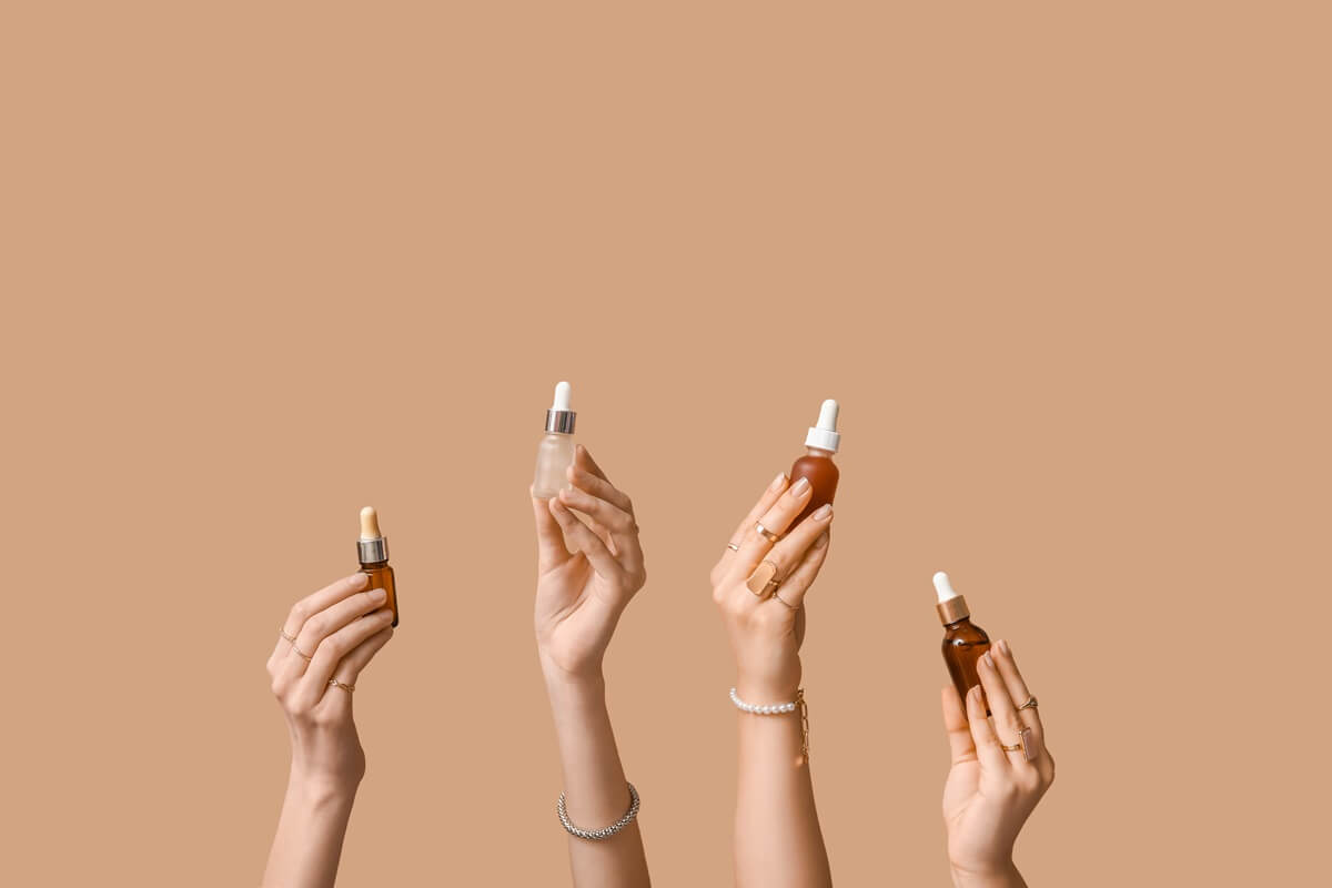 Ręce trzymające buteleczki z pipetą – produkty do pielęgnacji twarzy pokazujące, z czym łączyć kwas hialuronowy.