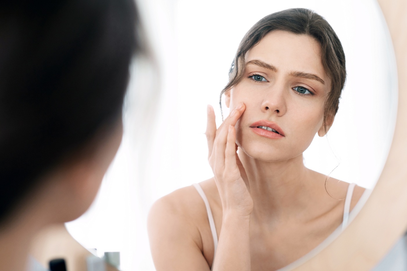 Zmartwiona kobieta ogląda w lustrze swoją skórę na policzku.