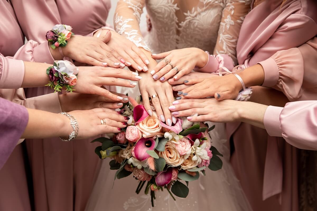 Kobiece dłonie - panny młodej i druhen w różowych szlafrokach skrzyżowane na środku eksponują manicure na wesele.