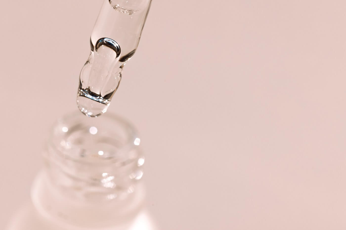 Pipeta z serum nad otwartą butelką kosmetyku do pielęgnacji skóry.