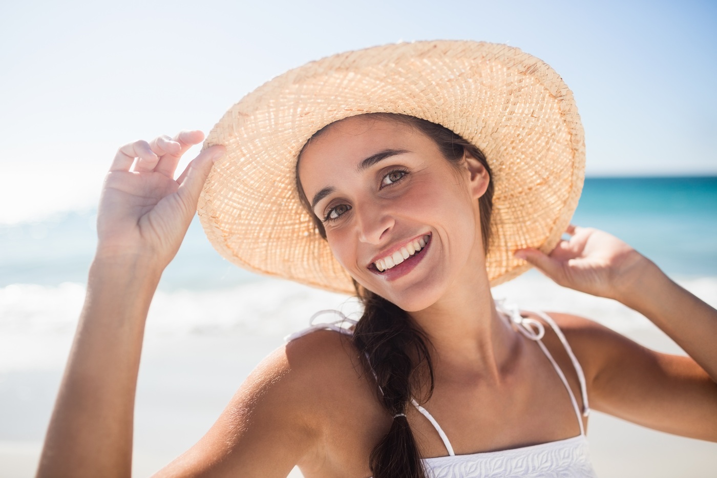 Portret uśmiechniętej kobiety na plaży, która w słomkowym kapeluszu.
