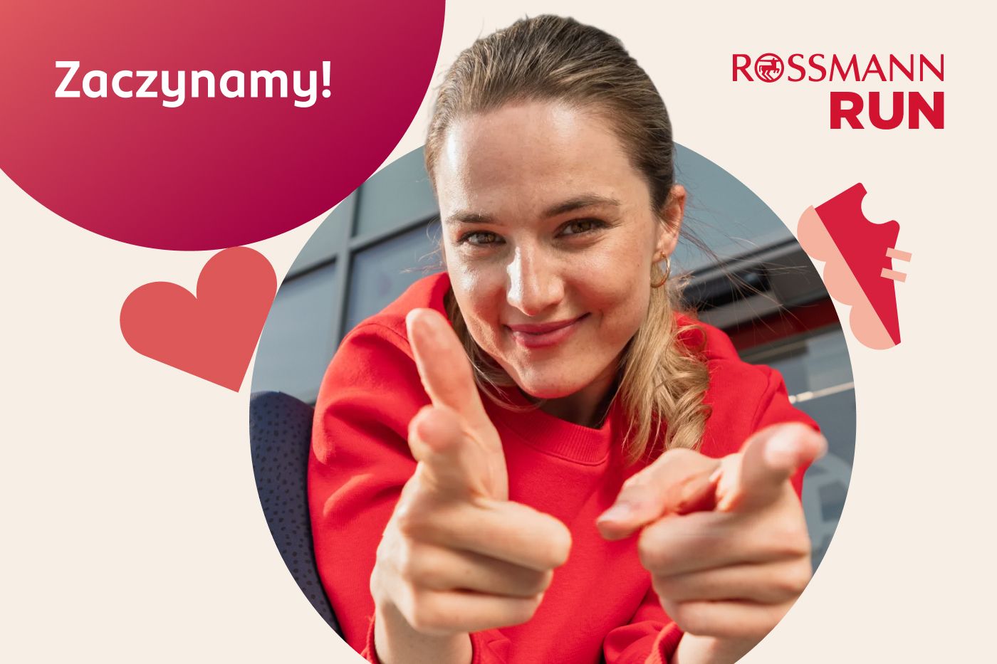 Uśmiechnięta kobieta w czerwonej bluzie wskazująca palcami w stronę odbiorcy, grafika promocyjna Rossmann Run.