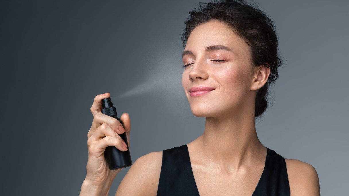 Kobieta rozpyla spray utrwalający na twarz po wykonaniu makijażu.