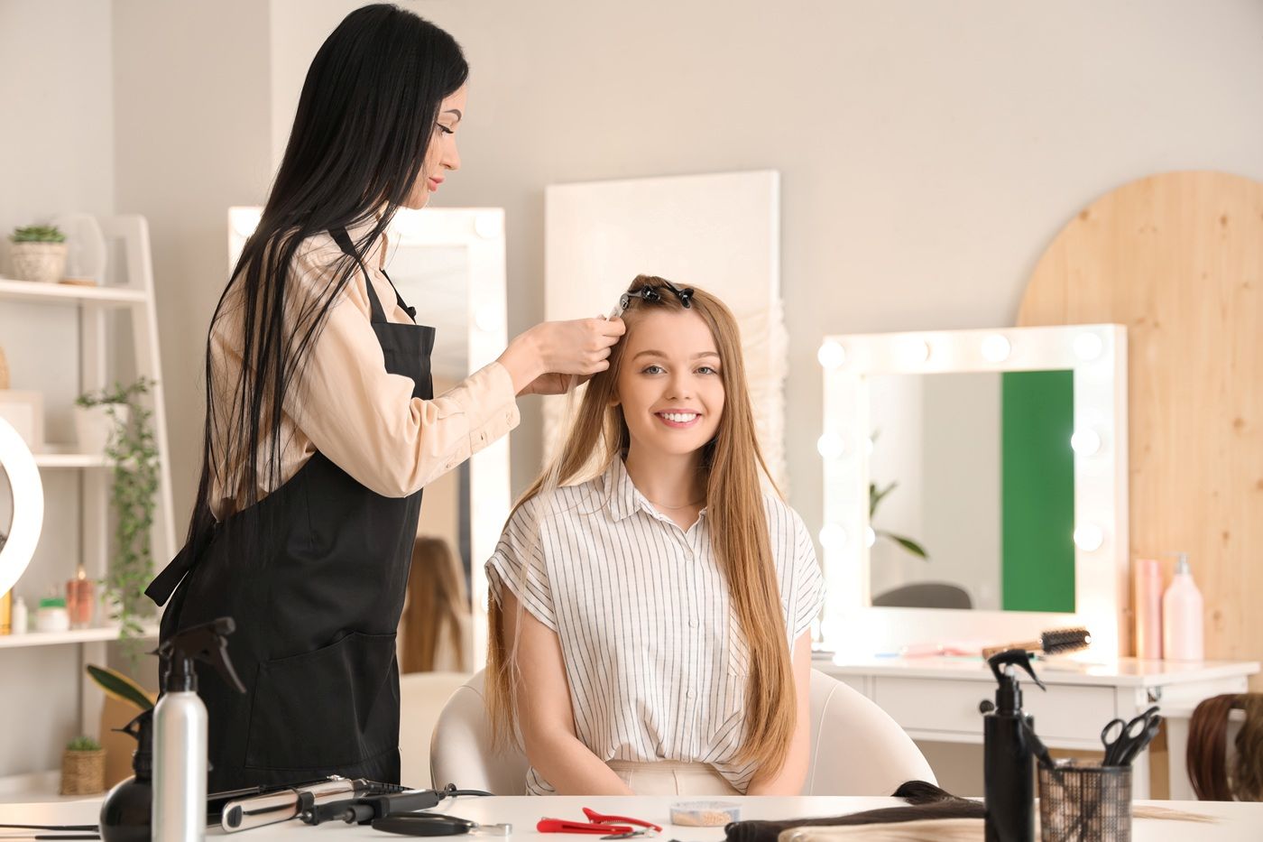 Fryzjerka przedłuża włosy młodej kobiecie siedzącej w fotelu w jasnym salonie fryzjerskim