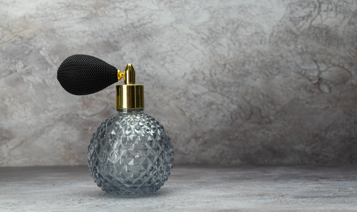Klasyczny flakon perfum z ozdobnego, tłoczonego szkła z czarną gruszką–atomizerem i złotą szyjką.